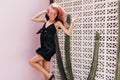 Happy girl with tanned skin dancing in summer black dress. Pink-haired woman jumping near cactus an Royalty Free Stock Photo