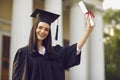 Happy girl university graduate standing and holding diploma in raised hand expressing happy celebration Royalty Free Stock Photo