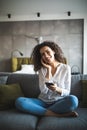 Happy young girl using her smartphone on the couch at home in the living room Royalty Free Stock Photo
