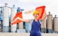 Happy girl in work clothes and hardhat with flag of peru standing in front of industrial scenery