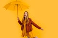 Happy girl in a yellow dress and autumn jacket, laughing and having fun with a yellow umbrella, standing on a yellow background, Royalty Free Stock Photo