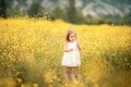 Happy girl in a yellow dress staying in the field of flowering rape. Nature blooms rape seed field