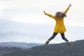 Happy girl in yellow jacket jumps with hands up to the sky on the top of mountains. Travel hiking and tourism Royalty Free Stock Photo