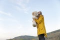 Happy girl in yellow park jacket tightly hugs soft bear toy stands on mountains background. Young woman with teddy bear Royalty Free Stock Photo
