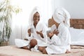 Happy girls in bathrobes sitting on bed and drinking coffee Royalty Free Stock Photo