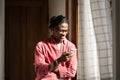 Happy glad African American hipster man in eyeglasses using smartphone standing near window at home. Royalty Free Stock Photo