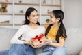 Happy glad korean millennial lady receives gift from teen daughter in living room interior, celebrate birthday