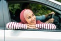 Happy glad young muslim man driving car with husband in hijab, lady looking out the window and enjoying car journey