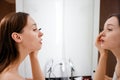 Happy glamour girl looking in mirror, applying mascara on eye lashes in bathroom. Young woman putting on cosmetic product for Royalty Free Stock Photo