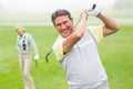 Happy golfer teeing off with partner behind him