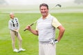 Happy golfer teeing off with partner behind him