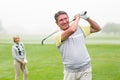 Happy golfer teeing off with partner behind him