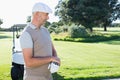 Senior man wearing flat cap gripping golf club on golf course beside golf cart, copy space Royalty Free Stock Photo