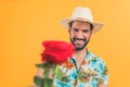happy good-looking Latin American man with a white hat holding a red rose orange background studio shot medium closeup Royalty Free Stock Photo