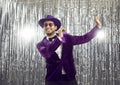 Happy goofy young man wearing a funny purple jacket and hat dancing at a disco party