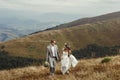 Happy gorgeous bride and groom walking in sun light holding han