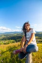 Happy gorgeous girl enjoy hills view sitting in flower field on the hill with breathtaking nature landscape Royalty Free Stock Photo