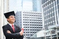 Happy graduate. Happy Asain man in graduation gowns holding diploma in hand on urban city background