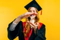 A happy graduate holds an hourglass in her hand on an isolated yellow background