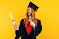 Happy graduate in a master`s dress, with a diploma on a yellow background. Concept of the graduation ceremony Royalty Free Stock Photo