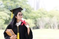 Happy graduate young Asian woman in cap and gown holding a book and certificated in hand, Education concept Royalty Free Stock Photo