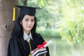 Happy graduate young Asian woman in cap and gown holding certificate and the book in hand, Education concept Royalty Free Stock Photo