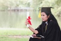 Happy graduate young Asian woman in cap and gown holding certificated in hand with commitment and pride, Education concept