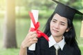 Happy graduate young Asian woman in cap and gown holding a certificated in hand, A diploma with red ribbon education concept in