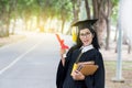 Happy graduate young Asian woman in cap and gown holding certificated in hand, Education concept