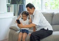 happy Grandfather and granddaughter Sharing smartphone together listening to music with headphone enjoying on sofa in living room