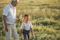 Happy grandfather and grandson walking at summer meadow.  Cute boy gives flowers his old grandpa Royalty Free Stock Photo