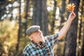 Happy grandfather holding yellow leaf over autumn leaves background. Senior man on a walk in a forest in an autumn Royalty Free Stock Photo