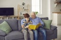 Happy grandfather reading book to his grandson while sitting on sofa in the living-room Royalty Free Stock Photo