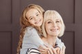 Happy grandmother and girl looking at camera over brown wall