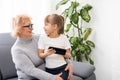 Happy grandmother and granddaughter using phone together, sitting on cozy sofa at home, browsing mobile device apps Royalty Free Stock Photo