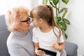 Happy grandmother and granddaughter using phone together, sitting on cozy sofa at home, browsing mobile device apps Royalty Free Stock Photo