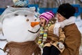 Happy grandmother and little granddaughter sculpt a big real snowman