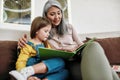 Happy grandmother reading book to granddaughter at home Royalty Free Stock Photo