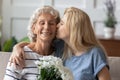Happy grandmother receiving tender kiss and flowers from grown granddaughter Royalty Free Stock Photo