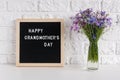 Happy grandmothers day text on black letter board and bouquet blue flowers in vase on table against white brick wall. Concept