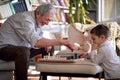 A happy grandpa at home enjoy teaching his little grandson how to play a chess. Family, home, playtime