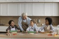 Happy grandpa and multiethnic grandsons in aprons preparing cookies