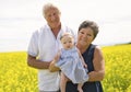 Happy grandparents with little baby granddaughter enjoying moment in beautiful yellow field