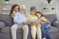 Happy grandparents and their two granddaughters look at a photo book with a family photo together. Royalty Free Stock Photo