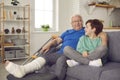 Happy grandson and his grandfather with broken leg in cast sitting on couch and talking Royalty Free Stock Photo