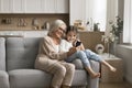 Happy granny cuddling sweet little tween grandkid girl with smartphone
