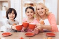 Happy granny with grandson and granddaughter clink cups of tea at kitchen. Royalty Free Stock Photo