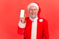 Happy gray bearded santa claus holding and showing smartphone with white display looking at camera with toothy smile