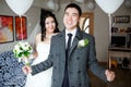 Happy groom with balloons in his hands, indoors at wedding day, the bride in the background.