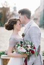 Happy groom kisses his gorgeous bride. Old city buildings and wedding decor on the background Royalty Free Stock Photo